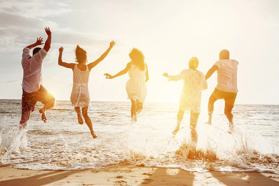 Group of people jumping joyfully in ocean waves at sunset on a Florida beach.
