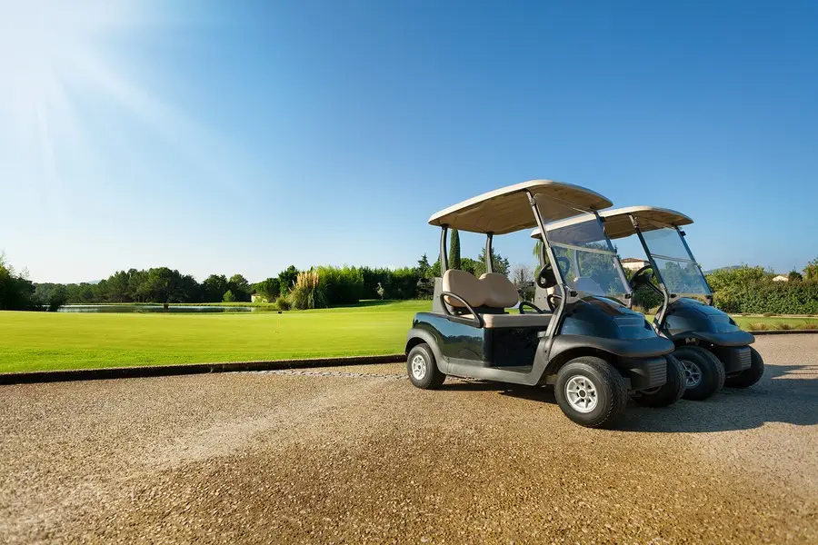 Two golf carts parked on a path beside a green golf course under a clear blue sky.