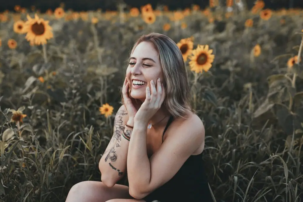 Smiling woman sitting in a sunflower field, hands on her face, radiating joy and hope in recovery.